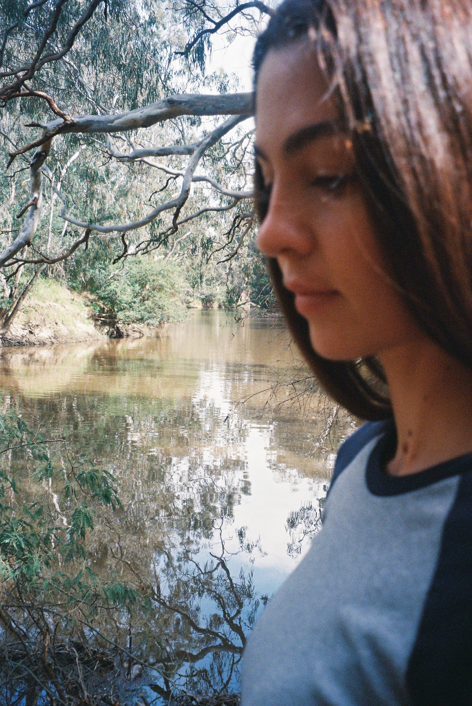 kita alexander in profile with eyes lowered, a still river behind her