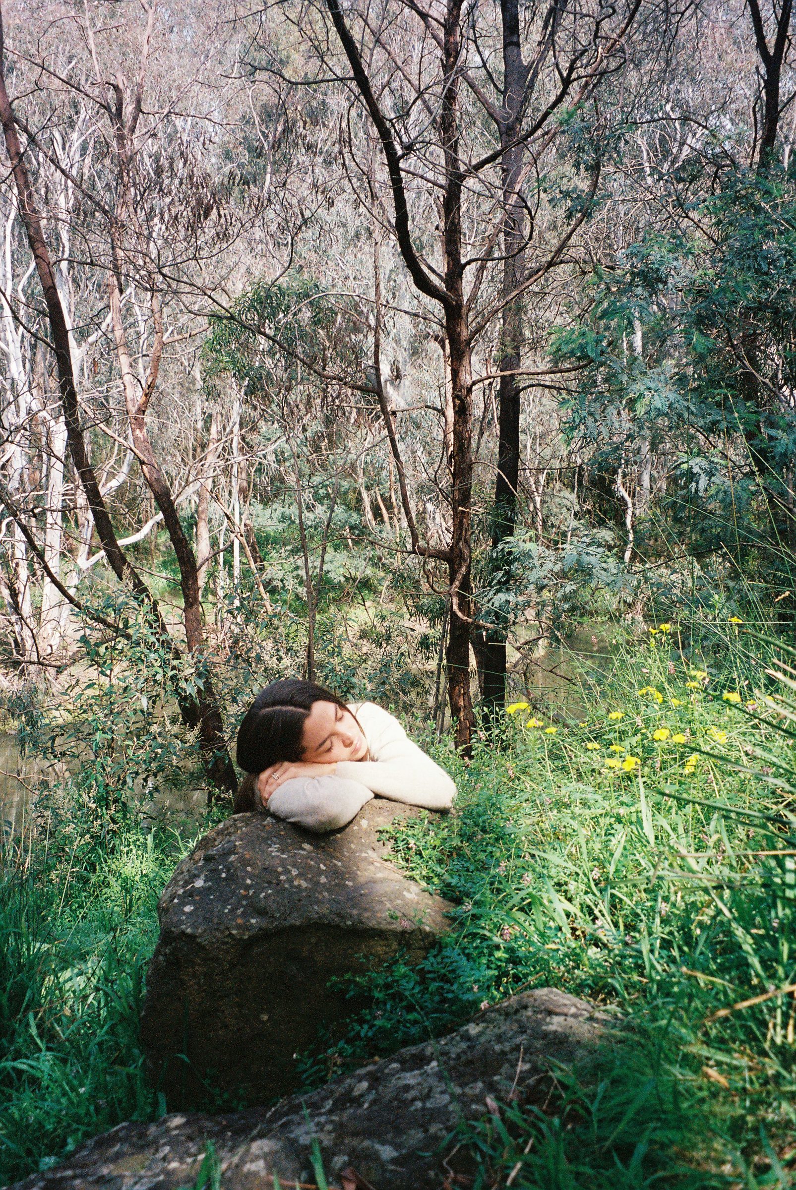 kita alexander resting her head on her folded arms on a mossy rock among wildflowers, eyes closed